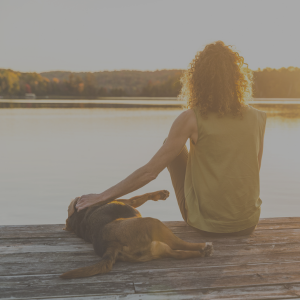 Retired woman sitting with her dog on the dock at sunset