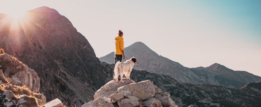 Woman and dog standing atop a mountain in the midst of a desert mountain range