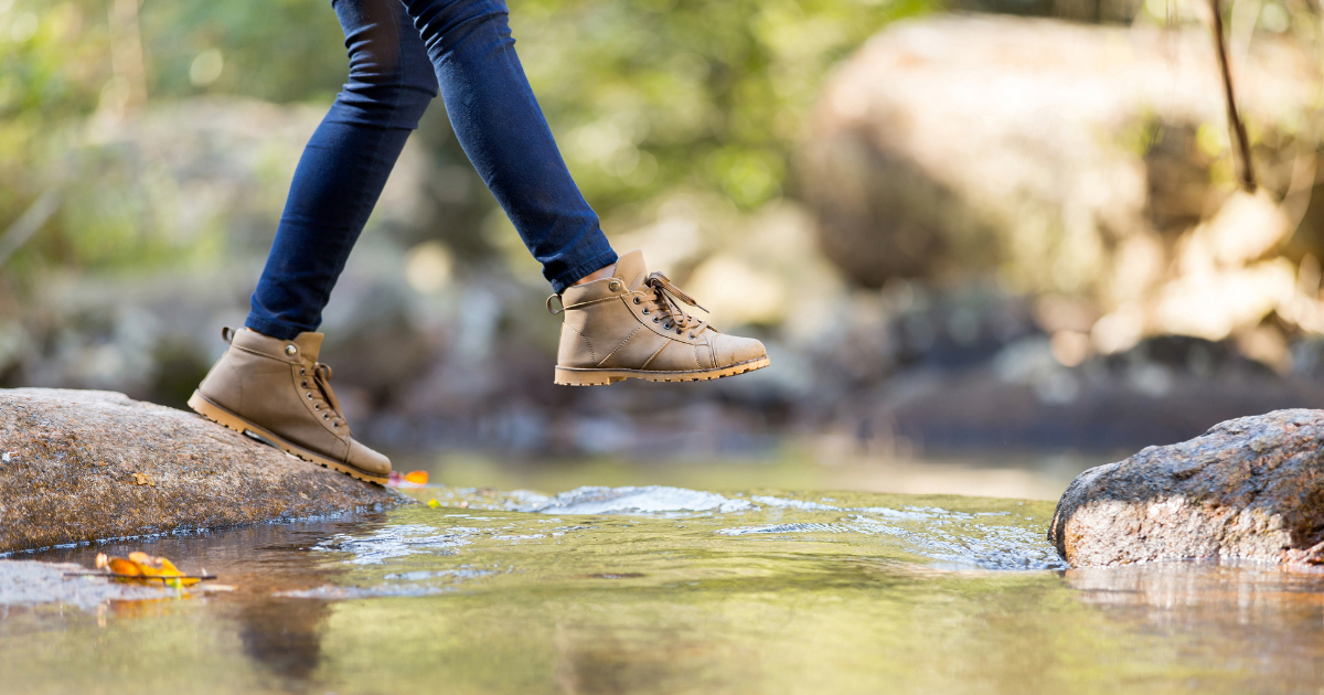 women taking a step over a stream