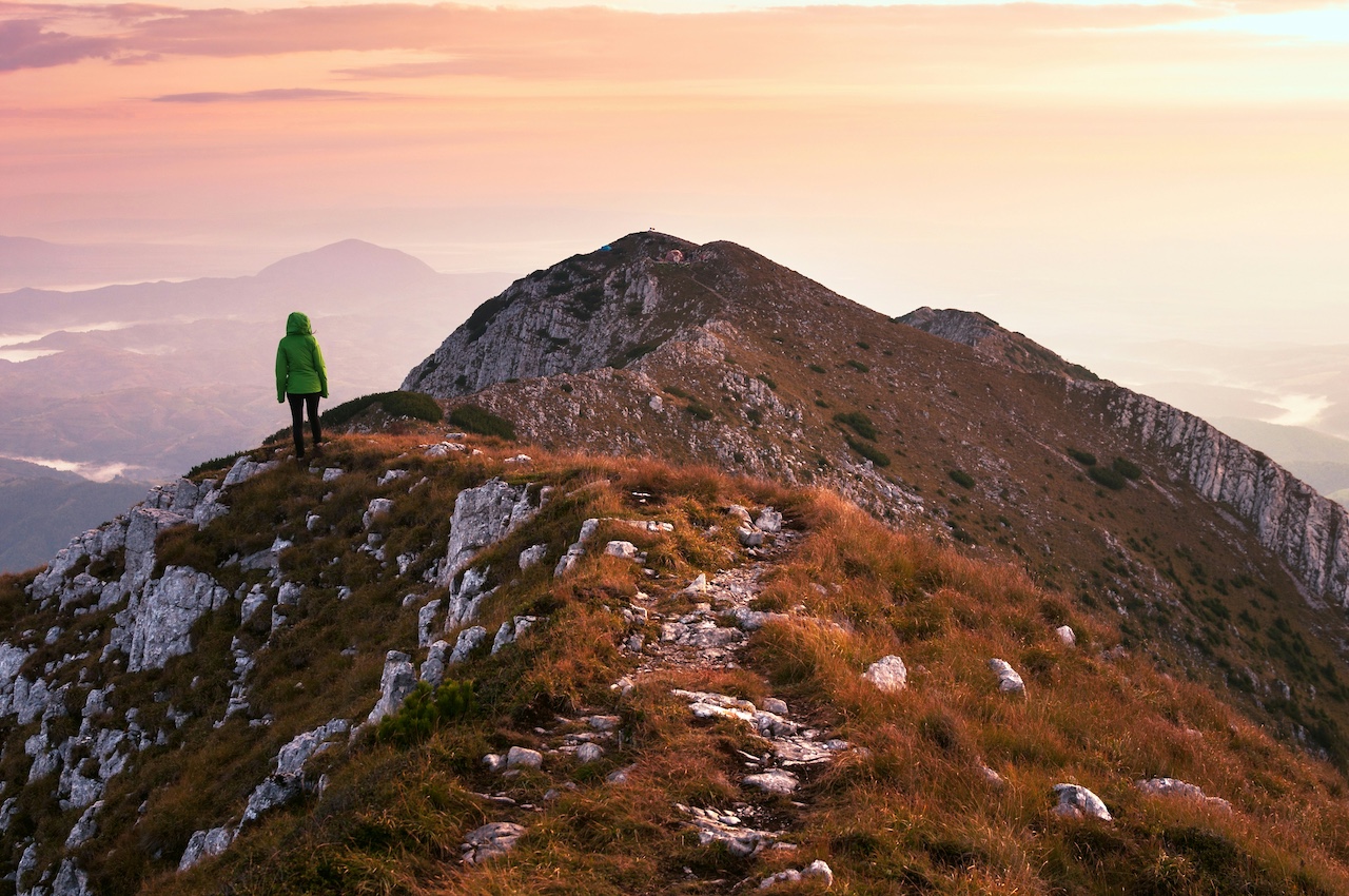 you woman standing on mountain side at sunset